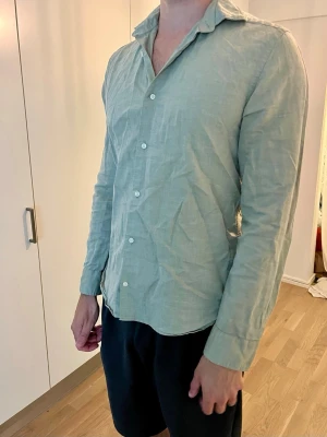 Ljusgrön/beige linneskjorta från Riley - Snygg ljusgrön skjorta från Riley i slim fit-modell. Tillverkad i ett luftigt linnematerial som passar perfekt för varmare dagar. Skjortan har långa ärmar, klassisk krage och vita knappar framtill.
