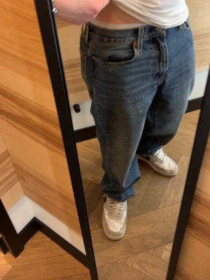Levi's 568 blå loose jeans - Klassiska blå Levi's 568 jeans med loose passform och femficksmodell. Jeansen har en mörk tvätt, tydliga sömmar och den ikoniska röda Levi's-lappen på bakfickan. Tillverkade i slitstark bomullsdenim och har läderpatch bak i midjan. Har små slitningar vid benen längst ner, sista bilden.