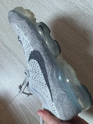 Nike Air Vapormax Flyknit grå - Nike Air Vapormax Flyknit sneakers i ljusgrått med svart Swoosh på sidan. Skorna är knappt använda och är som nya..