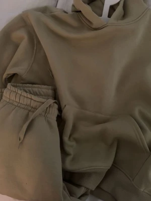 Beige mjukisset med hoodie och byxor - Säljer ett loungewear-set med hoodie och matchande byxor. Hoodien har en stor ficka framtill och ribbade muddar, medan byxorna har resår i midjan och dragsko. Perfekt för chill dagar hemma eller när du vill vara extra bekväm. Aldrig använda, köpta för 658kr