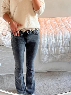 Svarta bootcut jeans med tvättad look - Säljer ett par svarta bootcut jeans med tvättad look och rå kant vid midjan. Jeansen har klassisk femficksmodell och normalhög midja. Snyggt slitna detaljer och stretchigt material för skön passform. 