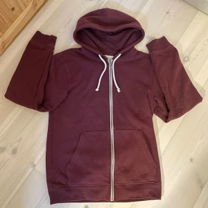 ZIP-HOODIE | PIER ONE. - Mysig vinröd hoodie med vit dragkedja och matchande vita snören i huvan. Hoodien har två stora fickor framtill och ribbade muddar vid ärmar och nederkant. Perfekt för en avslappnad stil och enkel att matcha med jeans eller mjukisbyxor.