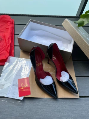 Svarta lackpumps från Christian Louboutin - Säljer ett par ikoniska svarta pumps från Christian Louboutin i glansigt lackläder. Skorna har spetsig tå, hög klack och den klassiska röda sulan. Insidan är röd med guldfärgad logga. Perfekta för dig som vill sticka ut med lyxig design. Fraktar direkt!