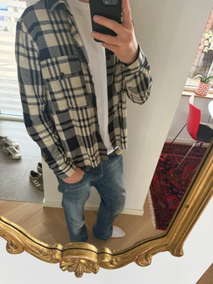 Vintage skjorta från A days merch  - Säljer en beige och mörkblå rutig skjorta med klassisk krage och två bröstfickor. Skjortan har långa ärmar och knäppning framtill. Perfekt för en avslappnad och trendig stil. Materialet känns mjukt och bekvämt.