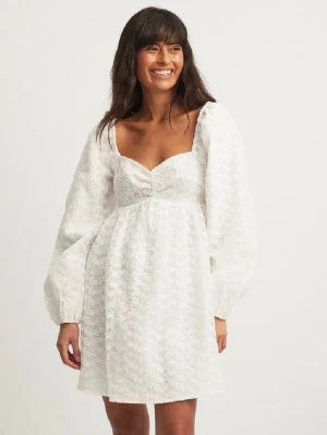 Vit spetsklänning från NA-KD - Supersöt vit kort klänning från lovisa wallin x NA-KD med långa ärmar och v-ringning. Klänningen har spetsdetaljer över hela tyget och en liten rosett framtill. Perfekt för sommarens alla tillfällen och ger en romantisk vibe. Använd 1 gång. 