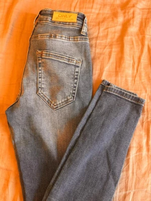 Blå skinny jeans från ONLY XS/32 - Säljer ett par blå skinny jeans från ONLY i modellen ONLBLUSH MID. Jeansen har klassisk femficksdesign, medelhög midja och är gjorda i stretchigt denimtyg för en bekväm passform. Perfekta till vardags och lätta att matcha med olika stilar. Har köpt den helt ny från ONLY butiken.