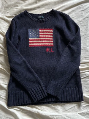 Mörkblå stickad tröja Ralph Lauren - Mörkblå stickad tröja från Ralph Lauren med amerikansk flagga och RL-broderi. Tröjan har rund hals, långa ärmar och breda ribbade muddar vid ärmslut och nederkant. Den är storlek L i barn (14-16 år) och passar mig som bär Xs-S. Nypris: 2395kr. 🩷