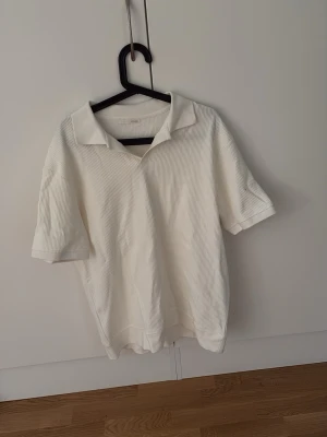 Vit ribbad skjorta från Zara - Vit kortärmad skjorta från Zara med ribbad struktur och klassisk krage. Skjortan har en relaxed fit och är tillverkad i ett mjukt material som känns skönt mot huden. Perfekt för en clean och stilren look.