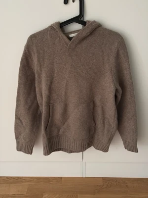Beige stickad hoodie från Zara - Mysig beige stickad hoodie från Zara i storlek M. Hoodien har en klassisk huva, magficka och ribbade muddar vid ärmslut och nederkant. Perfekt för en avslappnad och stilren look. Materialet känns mjukt och skönt mot huden.