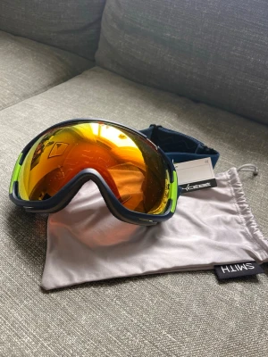 Cébé skidglasögon med spegelglas - Säljer ett par Cébé skidglasögon med spegelglas i orange/guldton. Ramen är mörkblå med limegröna detaljer och ett elastiskt band med Cébé-logga. Medföljer en vit förvaringspåse från Smith. Perfekta för vinterns äventyr i backen.