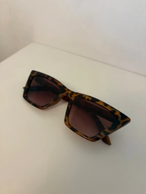 Leopardmönstrade solglasögon - Snygga solglasögon med breda, kantiga bågar i leopardmönster och mörka linser. Perfekt för dig som vill sticka ut och addera lite edge till din look. Bågarna är i syntetmaterial och har en cool retrovibe.