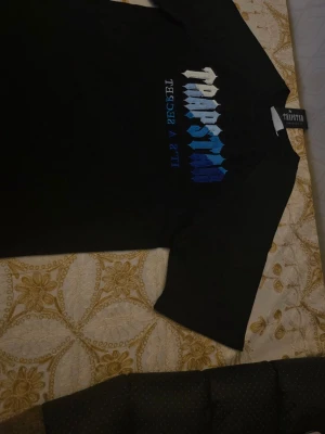 Trapstar svart t-shirt med blått tryck - Trapstar T-shirt – Svart/Blå (Strl M) Säljer en populär Trapstar T-shirt i svart med blå/vit logga. Helt ny med tags kvar. • Storlek: M (normal passform) • Skick: Ny med tags • Färg: Svart med blå/vit logga • Väldigt eftertraktad modell • Säljs ofta för betydligt högre priser på nätet Passa på att fynda innan den blir såld.
