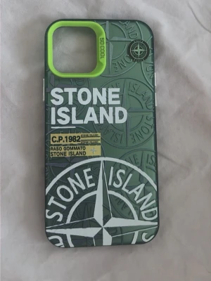 Grönt Stone Island mobilskal - Snyggt mobilskal i grönt med Stone Island-logga och detaljer i vitt och gult. Skalet har en unik design med upphöjd limegrön ram runt kameran och tydliga tryck. Tillverkat i tåligt plastmaterial och passar perfekt för dig som vill ha en streetwear-inspirerad look. Pris kan diskuteras