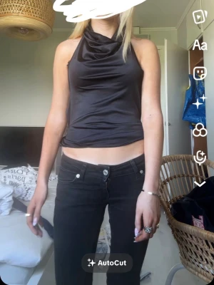 Svart halterneck topp i satin - Snygg svart halterneck topp i glansigt satinmaterial med draperad halsringning. Toppen är croppad och ärmlös, perfekt för att lyfta din outfit med en trendig touch.