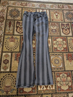 Gråa randiga bootcut jeans - Säljer ett par gråa jeans med breda vertikala svarta ränder. Modellen har bootcut-ben och klassiska fem fickor. Jeansen har bälteshällor och knappgylf. Materialet känns som bomullsdenim med lite stretch. W29 L34. Passar någon som är 170 lång. 