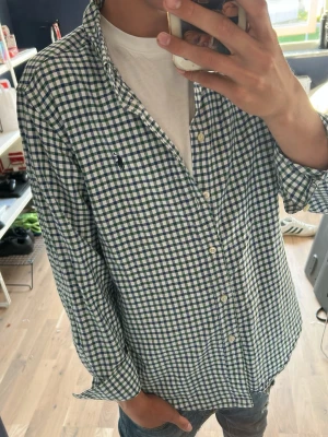 Rutig skjorta från Ralph Lauren - Klassisk rutig skjorta från Ralph Lauren i blått, grönt och vitt. Skjortan har lång ärm, knappar framtill och en liten broderad logga på bröstet. Tillverkad i mjuk bomull och har en avslappnad passform som funkar till många olika stilar.