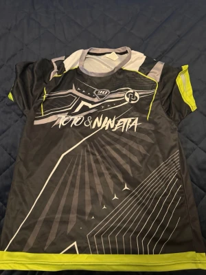 JUL T-shirt  - Säljer en svart och grå sporttröja från Toto & Ninjetta med gula detaljer och grafiskt tryck. Tröjan har korta ärmar, nummer 7 på ryggen och är tillverkad i ett lätt, ventilerande material som passar perfekt till träning eller match.
