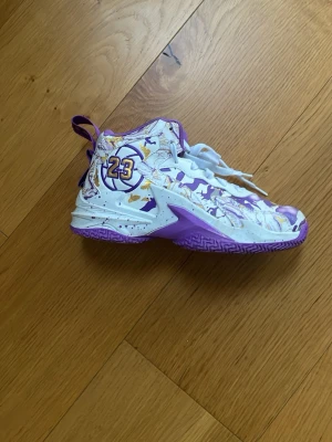 Basketkängor/Idrottsskor Lebron James  - Säljer ett par höga basketkängor med coolt vitt, lila och guldmönster. Skorna har nummer 23 på sidan och lila sula med greppmönster. De har vita snören och detaljerade paneler, perfekta för dig som vill sticka ut på planen. Tar emot byten 