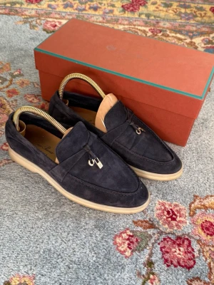 Loro Piana Summer Charms Walk - Snygga mörkblå loafers i mocka från Loro Piana med ljus sula och dekorativ metall-detalj framtill. Skorna har klassisk form och är perfekta för dig som gillar stilrena och exklusiva skor. Levereras med originalkartong. Slutsålda överallt, i alla färger.