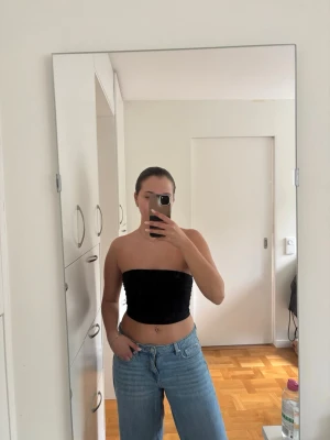 Svart bandeau tubtopp i sammet - Säljer en svart bandeau tubtopp med rynksöm vid sidorna. Toppen är axelbandslös och tight i passformen, perfekt att styla med höga jeans eller kjol. 