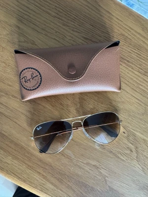 Ray-Ban pilot solglasögon guld - Snygga Ray-Ban aviator solglasögon med guldfärgade metallbågar och mörktonade glas. Klassisk pilotmodell, knappt använda! Mycket bra skick! Kommer med original brunt fodral med Ray-Ban-logga. Orginal pris: 1490kr