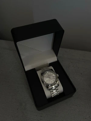 Silverfärgad klocka från Lige - Stilren klocka i silverfärg med klassisk länkarmband och rund urtavla. Specifikationer: Storlek: 39mm Urverk: NH35 (Automatiskt) Material: 904L Rostfritt Stål Glas: Sapphire Glas  Tavla: Silver med stavindex Bezel: Räfflad Armband: Presidential Krona: Screw Down Vattentålighet: 30 Meter