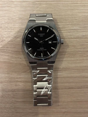 Tissot PRX Powermatic 80 klocka - Snygg Tissot PRX Powermatic 80 klocka i rostfritt stål med svart urtavla och datumvisning. Klockan har en klassisk länkarmband och stilren design som passar perfekt till alla outfits. Automatisk urverk och tydliga indexmarkeringar.✅ Helt ny och fortfarande plastad ✅ Inga skador, repor eller fel ✅ Aldrig använd (OPS box tillkommer ej) pris kan diskuteras 🤗 hör av er vid eventuella frågor 🧐😊