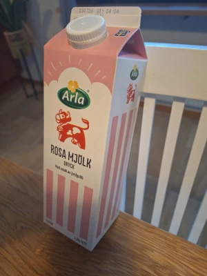 Arla Rosa Mjölk - bara förpackning  - En 1-liters förpackning Arla Rosa Mjölk Kartongen är rosa och vit med ränder och har en illustration av en rosa ko. Produkten är lågfett och har skruvkork på toppen.
