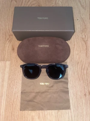 Svarta solglasögon från Tom Ford - Snygga svarta solglasögon från Tom Ford med klassisk design. Bågarna är tillverkade i Italien och har en elegant, stilren look. Kommer med originalfodral och putsduk med Tom Ford-logga.