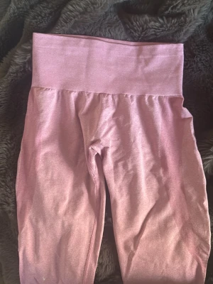 Rosa seamless leggings från NVGTN - Säljer ett par rosa seamless leggings från NVGTN med hög midja och stretchigt material. De har en bred midjeresår och diskret logga bak. Perfekta för gymmet eller chill dagar. Materialet är mjukt och följsamt för maximal komfort.