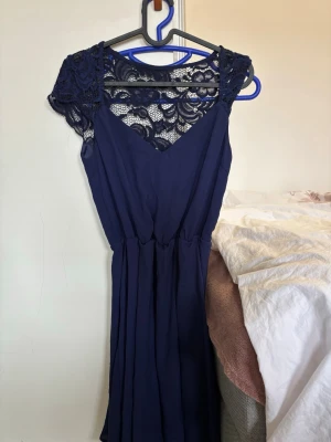 Marinblå långklänning med spets - Elegant marinblå midklänning med vacker spets upptill och vid axlarna. Klänningen har ett flytande fall och markerad midja. Perfekt för dig som vill ha en stilren och feminin look. Lite smuts på insidan, tas bort vid tvättning.