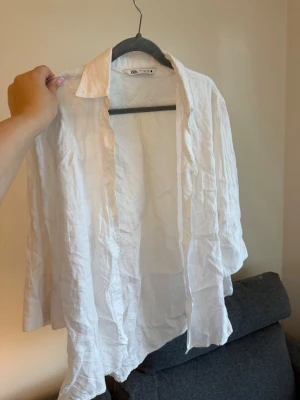 Vit linneskjorta från Zara - Säljer en luftig vit skjorta från Zara i linne. Skjortan har klassisk krage, knappar framtill och långärmad design. Perfekt för dig som gillar en avslappnad och stilren look. 