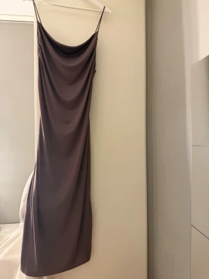 Lång brun slipklänning med tunna band - En helt ny oanvänd Zara klänning som är köpt för runt 600kr.  elegant långklänning i brun nyans med tunna axelband och draperad urringning. Klänningen har en smal passform och är tillverkad i ett mjukt, slätt material som ger ett stilrent intryck. Perfekt för dig som gillar minimalistisk och trendig stil. Klänningen är i storlek L men passar även mig som har storlek M. Klänningen kan se lila i vissa effekter. 