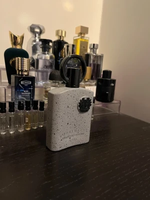 Afnan Supremacy Collector's Edition parfym - Unik parfymflaska från Armani Sì Collector's Edition. Flaskan är ljusgrå med svarta prickar och har en svart dekorativ blomma framtill samt en stor svart rund kork. Modern och stilren design som sticker ut i parfymhyllan.