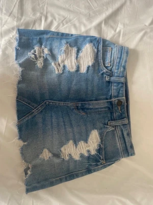 Blå jeanskjol med slitningar - Säljer en kort blå jeanskjol från hollister. Den är i storlek w23 och passar en xs. Den är i mycket fint skick. Pris kan diskuteras.