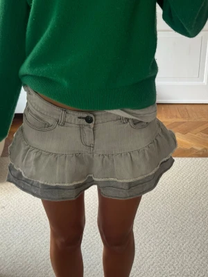 Grå volangkjol från Diesel - Supersöt grå minikjol från Diesel med volangkant och broderad fjäril på bakfickan. Kjolen har klassiska jeansdetaljer som bälteshällor, knapp och fickor fram och bak. Perfekt för dig som gillar en edgy och lekfull stil.