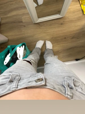 Ljusgråa slitna jeans med hål - Storlek 25/30. Säljer ett par ljusgråa jeans med raka ben och slitna detaljer på båda benen. Jeansen har hål vid knäna och klassisk femficksmodell. Perfekta för en avslappnad och trendig look. Materialet är denim i bomull.