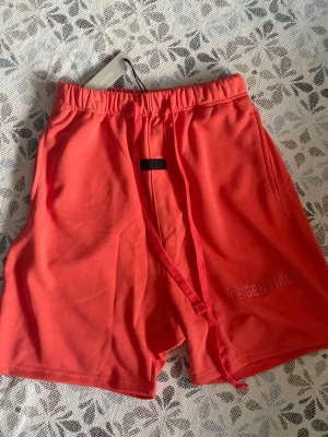 Koralröda shorts från Essentials - Koral essentials shorts, helt nya och oanvända i storlek M, hör gärna av vid frågor!