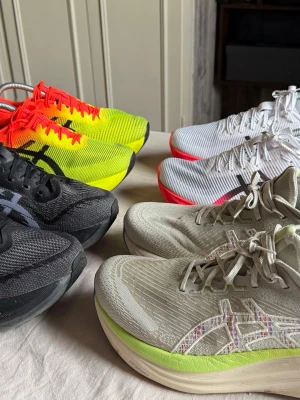 Asics sneakers i olika färger - Flera par Asics sneakers med mesh-ovandel och tjock sula. Finns i färgerna svart, vit med röda detaljer, beige med limegrön sula samt gul med orange detaljer. Klassisk Asics-logga på sidan och snörning framtill. Perfekta för dig som gillar sportig stil. (Man/ Unisex) 