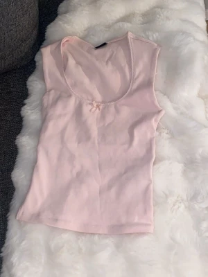 Ljusrosa ribbad linnetopp Gina Tricot - Supersöt ljusrosa ribbad linnetopp från Gina Tricot med rundad urringning och en liten rosett framtill. Perfekt att styla med jeans eller kjol för en enkel men gullig look. Aldrig använd. 💓💓💓