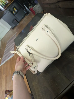 Sansibar handväska i beige - Säljer en elegant och stilren handväska från Sansibar i en vacker beige/cremefärgad nyans. Väskan är både praktisk och snygg, med flera fack som gör det enkelt att organisera dina saker.  ✨ Nypris: 1100 kr ✨ Från Sansibar ✨ Avtagbar och justerbar axelrem ✨ Flera fack med dragkedjor ✨ Silverfärgade detaljer ✨ Rymlig men smidig att bära  Väskan är sparsamt använd och i mycket fint skick. Perfekt till både vardag, arbete och festligare tillfällen.  📦 Skickas snabbt eller kan hämtas enligt överensko