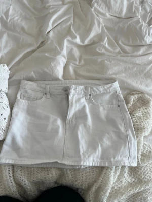 Vit jeanskjol med fickor - Snygg vit kort jeanskjol med klassiska fem fickor och bälteshällor. Kjolen har en rak passform och stängs med knapp och dragkedja framtill. Perfekt att matcha med en crop top eller stickad tröja.