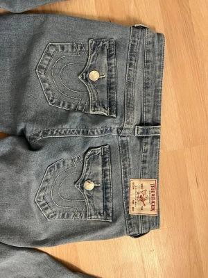 Bootcut jeans från True Religion - Säljer ett par ljusblå bootcut jeans från True Religion med klassiska kontrastsömmar och snygga fickdetaljer bak. Jeansen låg  midjade och är tillverkade i denim med lätt stretch för skön passform.