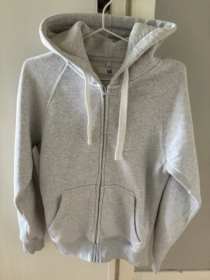 Ljusgrå hoodie från Russemerch - Ljusgrå zip-hoodie från Russedress med vit dragkedja och vita snören i huvan. Hoodien har känguruficka framtill och ribbade muddar vid ärmar och nederkant. Tillverkad i mjuk bomullsblandning, perfekt för chill dagar. Nypris 749kr