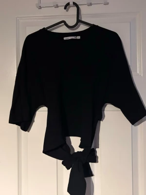 Svart croppad topp med knyt - Säljer en svart croppad topp med snygg knytning baktill. 