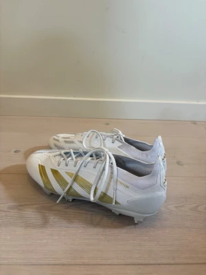 Adidas Predator Elite FG Day spark-vit/guld - Säljer ett par snygga Adidas predator fotbollsskor i vitt med guldiga detaljer och klassiska ränder. Anvönda ett fåtal gånger och påse kommer till (se bild). Strolek 40. Nypris: 2999 kr.