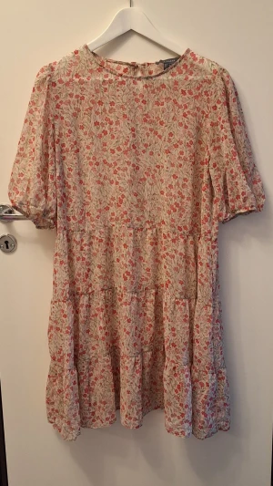 Blommig kortklänning från Primark - Söt kortklänning från Primark med blommigt mönster i rött och grönt på beige botten. Klänningen har puffiga kortärmar och är skir.