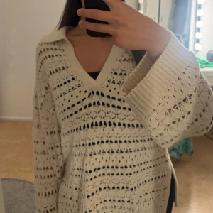 Beige stickad kofta med v-ringning - Säljer en beige stickad kofta med v-ringning och bred krage. Koftan har ett snyggt hålmönster och långa, vida ärmar med ribbade muddar. Perfekt för dig som gillar chill och cozy vibes. Passar till både jeans och kjol.