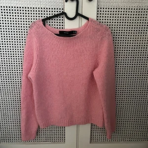 Rosa stickad tröja från Vero Moda - Mysig rosa stickad tröja från Vero Moda med rund hals och långa ärmar. Perfekt för att ge din outfit en färgklick och passar lika bra till jeans som till kjol. Tröjan har en mjuk och fluffig känsla och ribbade muddar vid ärmslut och nederkant.