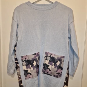 Ljusblå stickad klänning med camo-fickor - En ljusblå stickad klänning/oversize tröja med camouflage-mönster. Koreansk streetstyle som är snygg till shorts, jeans & leggings. 